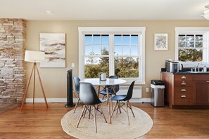A dining area with a round table, chairs, and a view through a large window. - Perch - Studio Retreat | Private Balcony | Sunset Views (Coupeville)