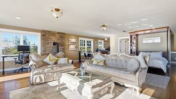 A spacious living room with a stone fireplace, a large sofa set, a coffee table, and a view of the outdoors.