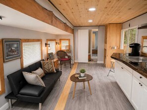 En moderne stue med en sort sofa, et sofabord og et spiseområde med en køkkenø.