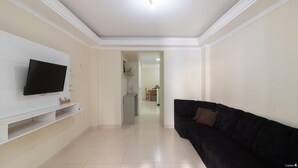 A living room with a flat-screen TV mounted on a white cabinet, a black sofa, and a tiled floor. - Apt With Balcony & BBQ 78m From the Beach Obs0101 (Itapema)