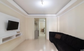 A living room with a flat-screen TV mounted on a white cabinet, a black sofa, and a tiled floor. - Apt With Balcony & BBQ 78m From the Beach Obs0101 (Itapema)