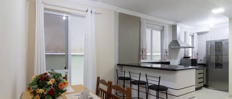 Ett modernt kök med en köksö i mitten, en matplats med stolar och ett kylskåp.