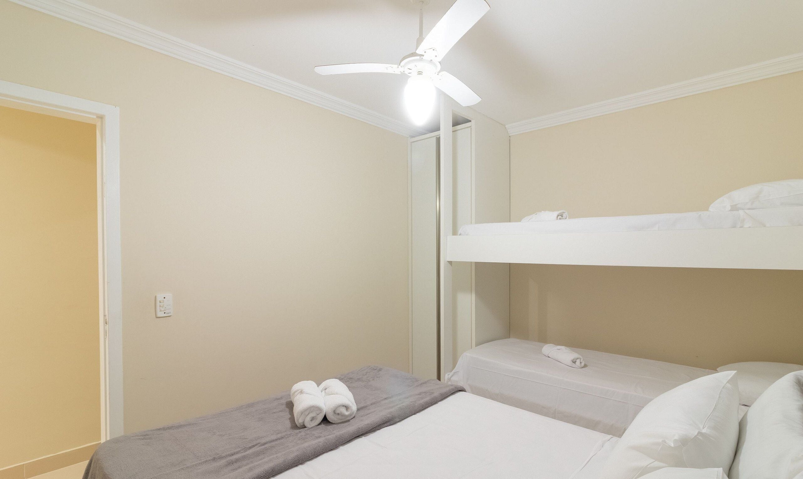 Piccola camera con un letto singolo, una ventola a soffitto, un asciugamano sul letto e uno specchio a parete.