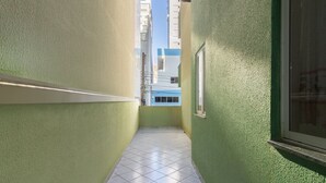 A narrow corridor with green walls and a tiled floor, leading to a window with a view of buildings. - Apt With Balcony & BBQ 78m From the Beach Obs0101 (Itapema)