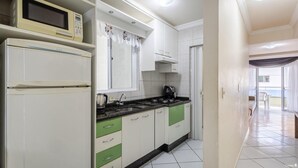 A kitchen with white cabinets, a microwave, a stove, and a window with decorative curtains. - Apt With Balcony Steps From the Beach - Obs0201 (Itapema)