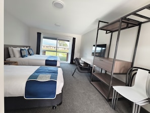Ein Hotelzimmer mit zwei Betten, einem Schreibtisch, einem Stuhl, einem Fernseher und einem Balkon mit Blick.