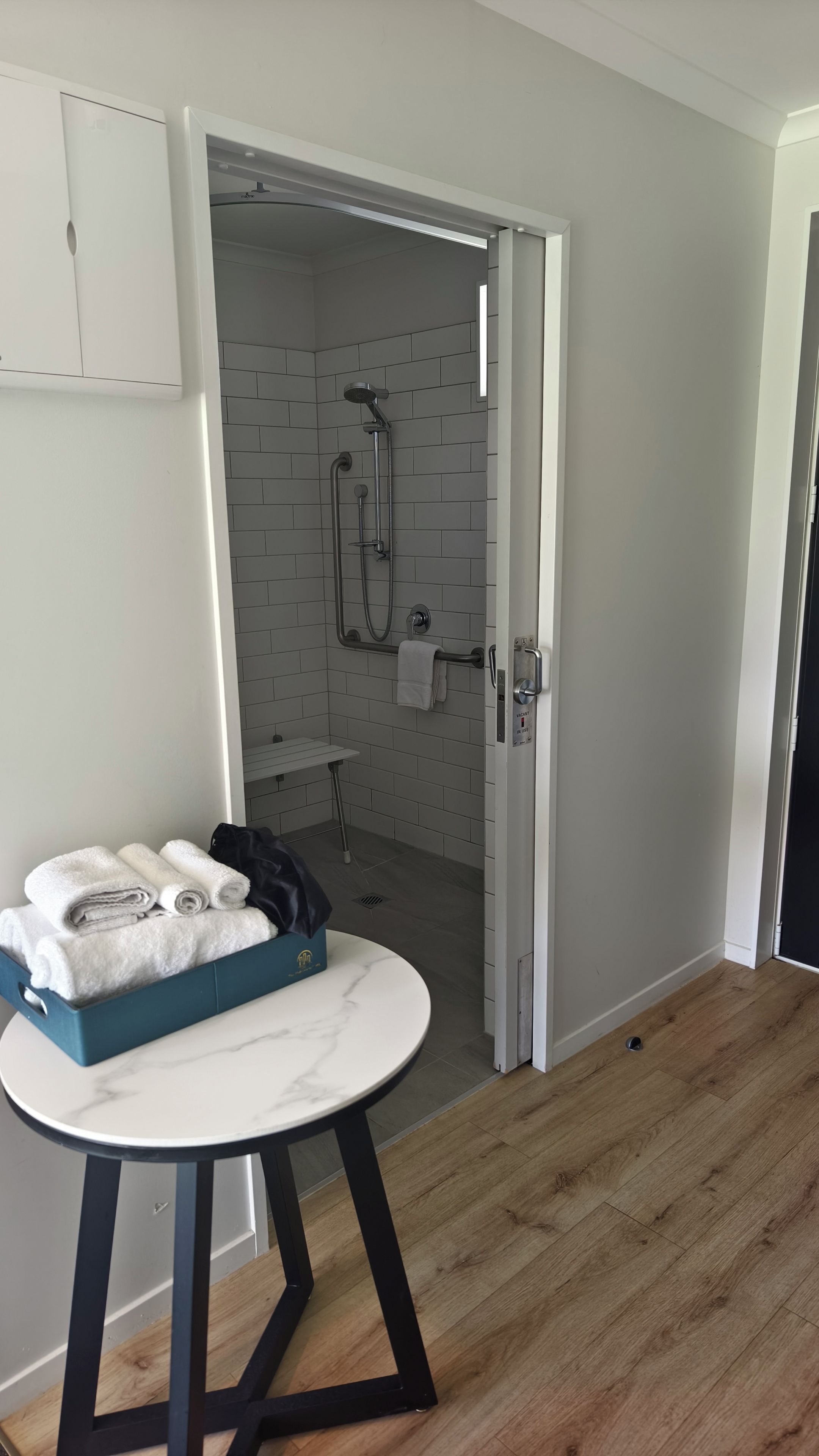 A bathroom with a shower, a towel rack, and a small table with towels.