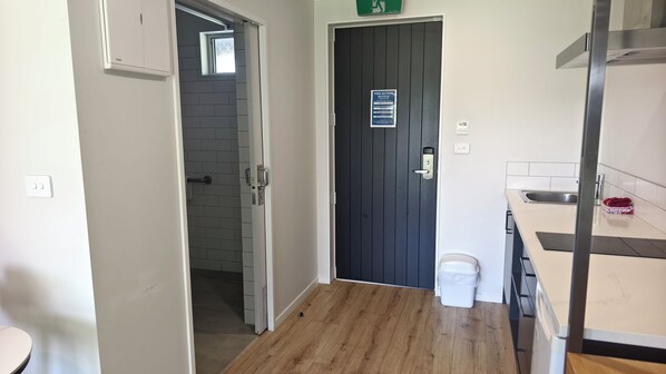A hallway with a dark door, a small window, and a white trash bin.