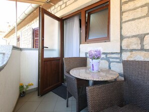 Een klein balkon met rieten meubilair, een tafel en een raam met gordijn.