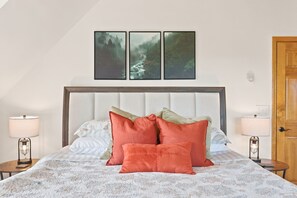Ein Schlafzimmer mit einem Bett, Kissen, einem Nachttisch, einer Lampe und einer Tür.