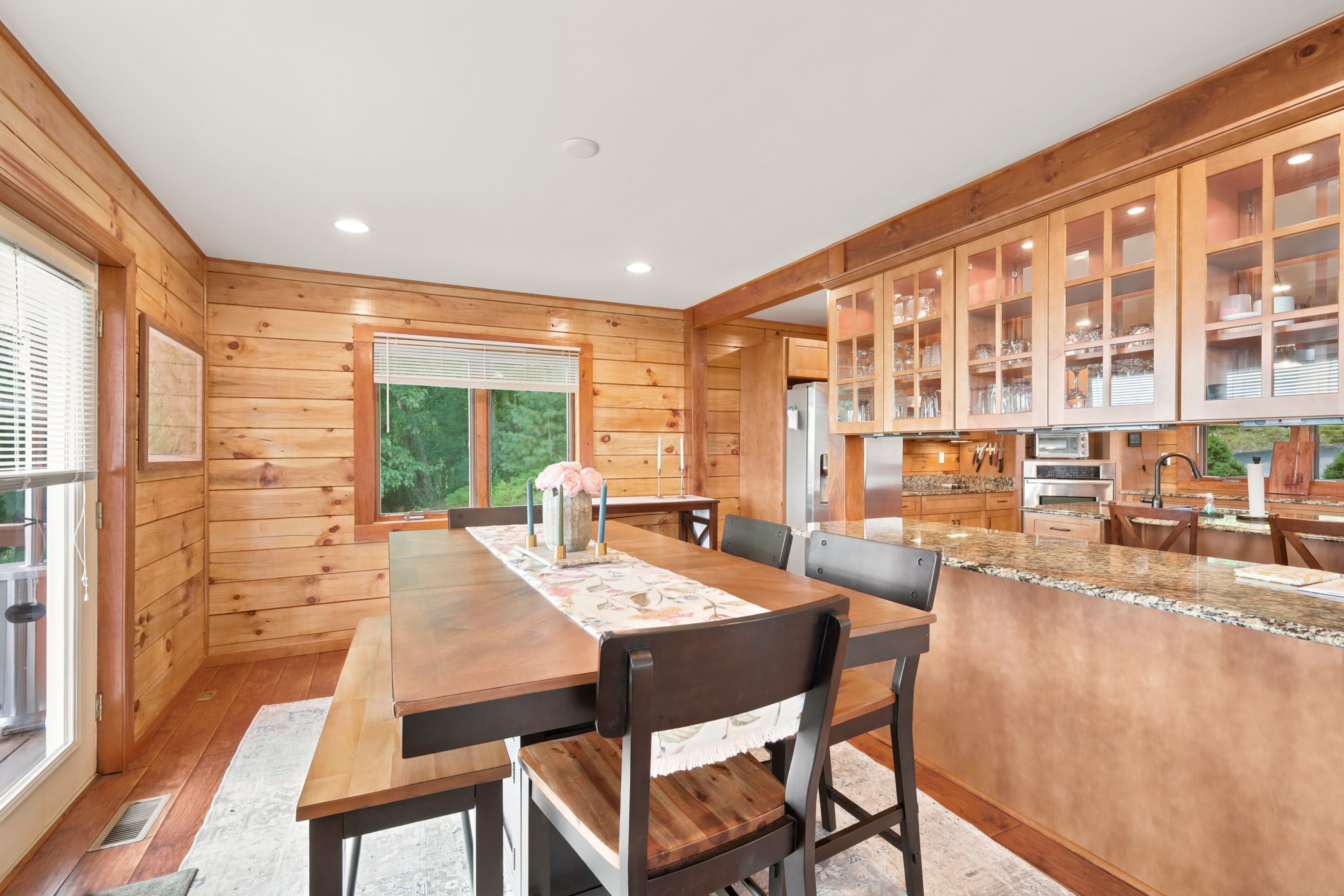 A wooden interior with a dining area, kitchen, and large windows.