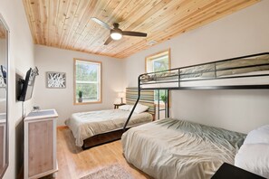 Ein Schlafzimmer mit Etagenbett, Schreibtisch, Stuhl, Deckenventilator und Fenstern mit Jalousien.