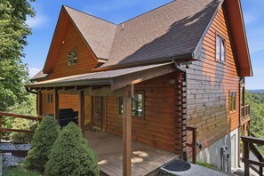 A two-story log cabin with a covered porch, a deck, and a view of the surrounding forest. - Parkway Place  4BR Boone Cabin · Long-Range Views · Hot Tub · Game Room (Boone)