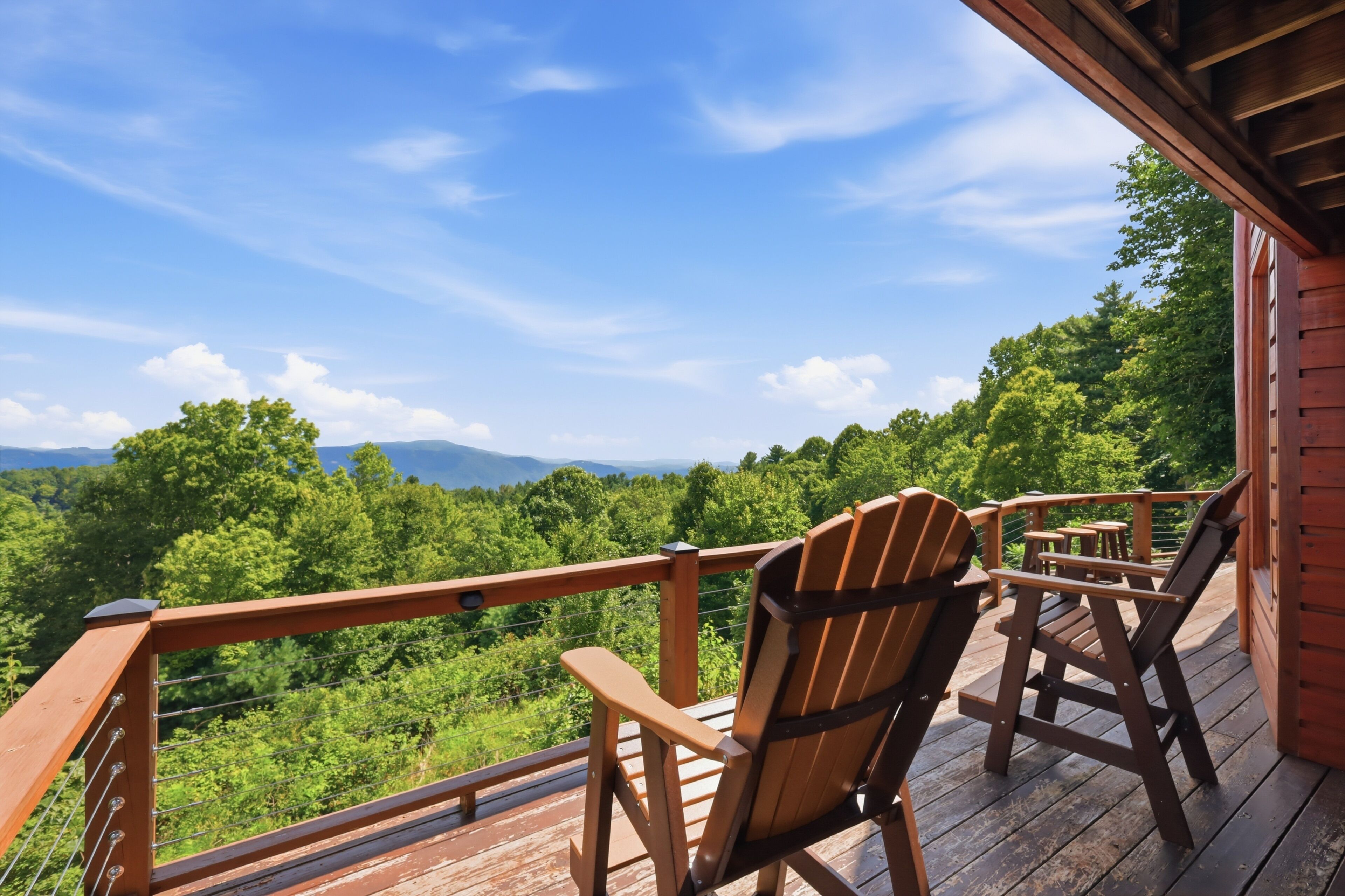 A wooden deck with Adirondack chairs overlooking a forested landscape.