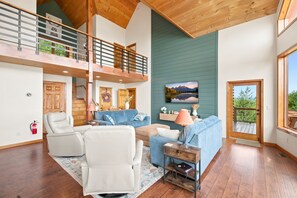 Amplia sala de estar con techo alto, vigas de madera, un sofá azul, un sillón blanco y una chimenea.