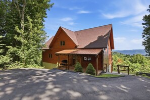 Ein Holzhaus mit schrägem Dach, einer Veranda und Blick auf den umliegenden Wald und die Berge.