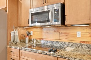 A kitchen with wooden cabinets, a stainless steel microwave, a granite countertop, and a built-in stovetop. - Parkway Place  4BR Boone Cabin · Long-Range Views · Hot Tub · Game Room (Boone)