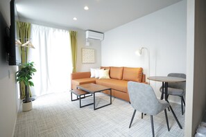 Ein modernes Wohnzimmer mit Sofa, Couchtisch, Beistelltisch, Stuhl und einem kleinen Tisch mit Lampe.