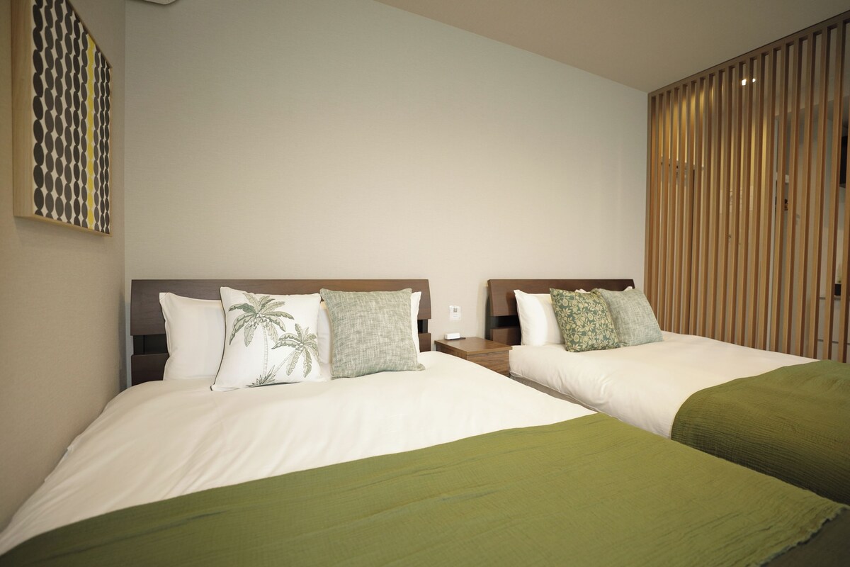 Ein Hotelzimmer mit zwei Betten, jeweils mit einem Kopfkissen und einer grünen Tagesdecke.