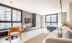 A modern living room with a sofa, dining table, chairs, and a TV. - Studio in Cond. w/ Pool in Floripa Ogd0704 (Florianópolis)