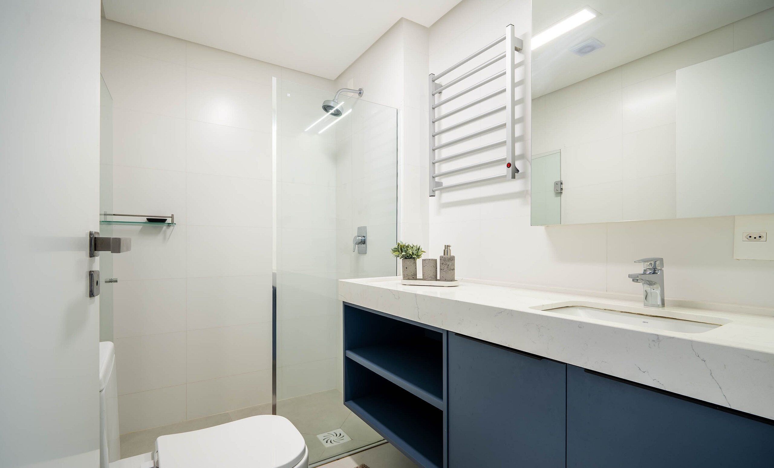 A modern bathroom with a glass shower enclosure, a white toilet, a marble sink, and a dark blue cabinet.