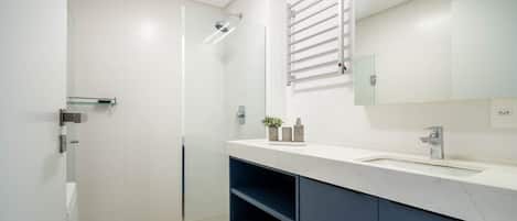 A modern bathroom with a glass shower enclosure, a white toilet, a marble sink, and a dark blue cabinet.