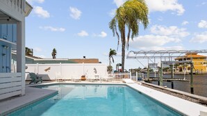 A swimming pool with lounge chairs, a white fence, and a view of a building and palm trees. - 5BR, 3BA, Heated Pool, Game Room, Firepit, Boat Dock on Hernando Beach (Hernando Beach)