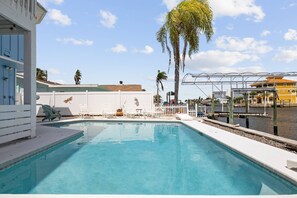 A swimming pool with lounge chairs, a white fence, and a view of a building and palm trees. - 5BR, 3BA, Heated Pool, Game Room, Firepit, Boat Dock on Hernando Beach (Hernando Beach)