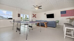 A room with a ping pong table, a ceiling fan, a TV, and a flag. - 5BR, 3BA, Heated Pool, Game Room, Firepit, Boat Dock on Hernando Beach (Hernando Beach)