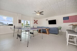 A room with a ping pong table, a ceiling fan, a TV, and a flag. - 5BR, 3BA, Heated Pool, Game Room, Firepit, Boat Dock on Hernando Beach (Hernando Beach)