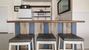 A kitchen with a wooden bar counter, three stools, a microwave, and a shelf with glassware. - 5BR, 3BA, Heated Pool, Game Room, Firepit, Boat Dock on Hernando Beach (Hernando Beach)