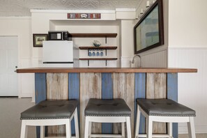 A kitchen with a wooden bar counter, three stools, a microwave, and a shelf with glassware. - 5BR, 3BA, Heated Pool, Game Room, Firepit, Boat Dock on Hernando Beach (Hernando Beach)