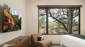 A bedroom with a large window, a bed, a chair, a wooden dresser, and a painting. - Signature Designer Home | Views, Wellness, Games (Sedona)