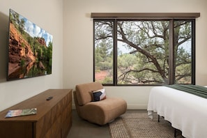 Quarto com uma grande janela, uma cama, uma cadeira, cômoda de madeira e um quadro.