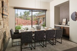 A dining area with a table set for four, surrounded by chairs, a stone wall, and a view of a landscaped garden. - Signature Designer Home | Views, Wellness, Games (Sedona)