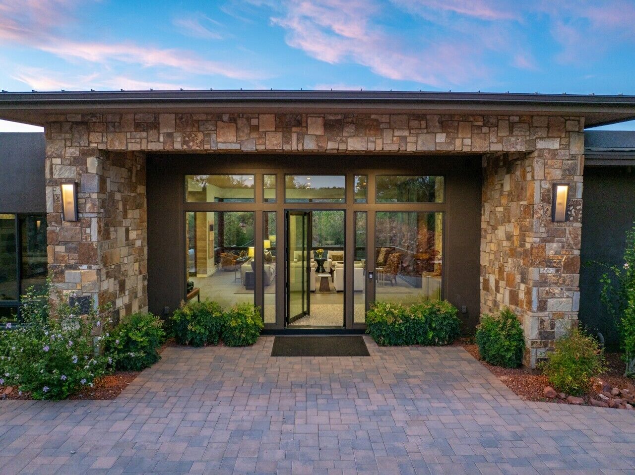 A modern building with a stone facade, large glass doors, and a paved entrance area.
