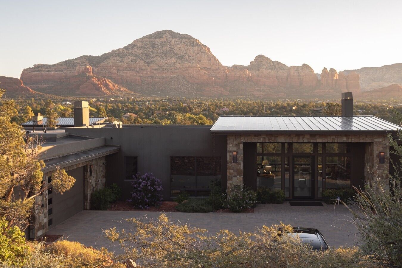 Una casa moderna con fachada de piedra, techo de metal y vista a un paisaje montañoso.