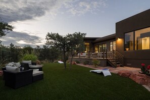 A modern house with a well-maintained lawn, outdoor seating, and a staircase leading to the entrance. - Signature Designer Home | Views, Wellness, Games (Sedona)