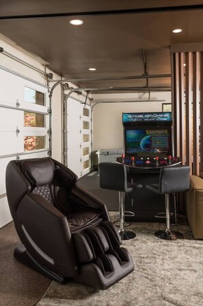 A massage chair, a gaming console, and a storage unit in a room with a garage door. - Signature Designer Home | Views, Wellness, Games (Sedona)