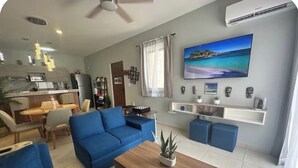 Een woonkamer met een blauwe bank, een salontafel en een televisie die aan de muur is bevestigd.