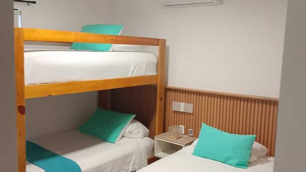 Een slaapkamer met een stapelbed, een plafondventilator, een nachtkastje en een wandairconditioner.