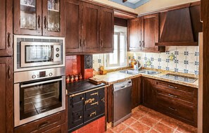 A kitchen with wooden cabinets, a built-in oven, a microwave, a dishwasher, and a tiled backsplash. - Amazing home in Iznajar (Iznajar)