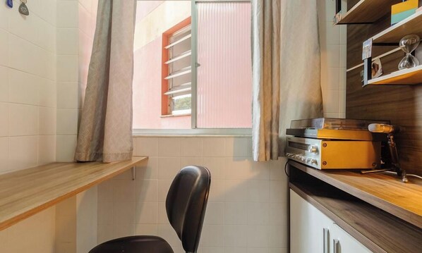 Una cocina compacta con ventana, una silla, una encimera y una estantería con objetos.