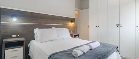 A neatly made bed with a gray blanket and a rolled towel, a bedside table with a lamp, and a wardrobe with a mirror.
