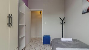 Un dormitorio con cama, perchero, maleta azul y armario.