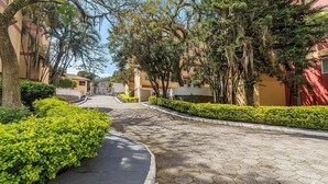 Un camino pavimentado bordeado por setos y árboles bien cuidados, que lleva a un edificio de fachada roja.