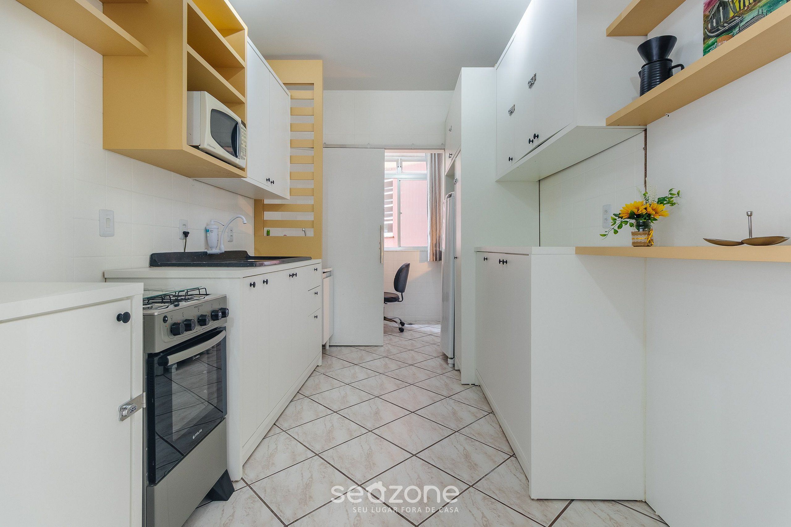 Una cocina compacta con armarios blancos, microondas, estufa y refrigerador.