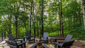 Un'area salotto all'aperto con poltrone Adirondack e un braciere, immersa in una foresta.