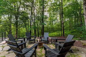 Un área de estar al aire libre con sillas Adirondack y un brasero rodeado de bosque.
