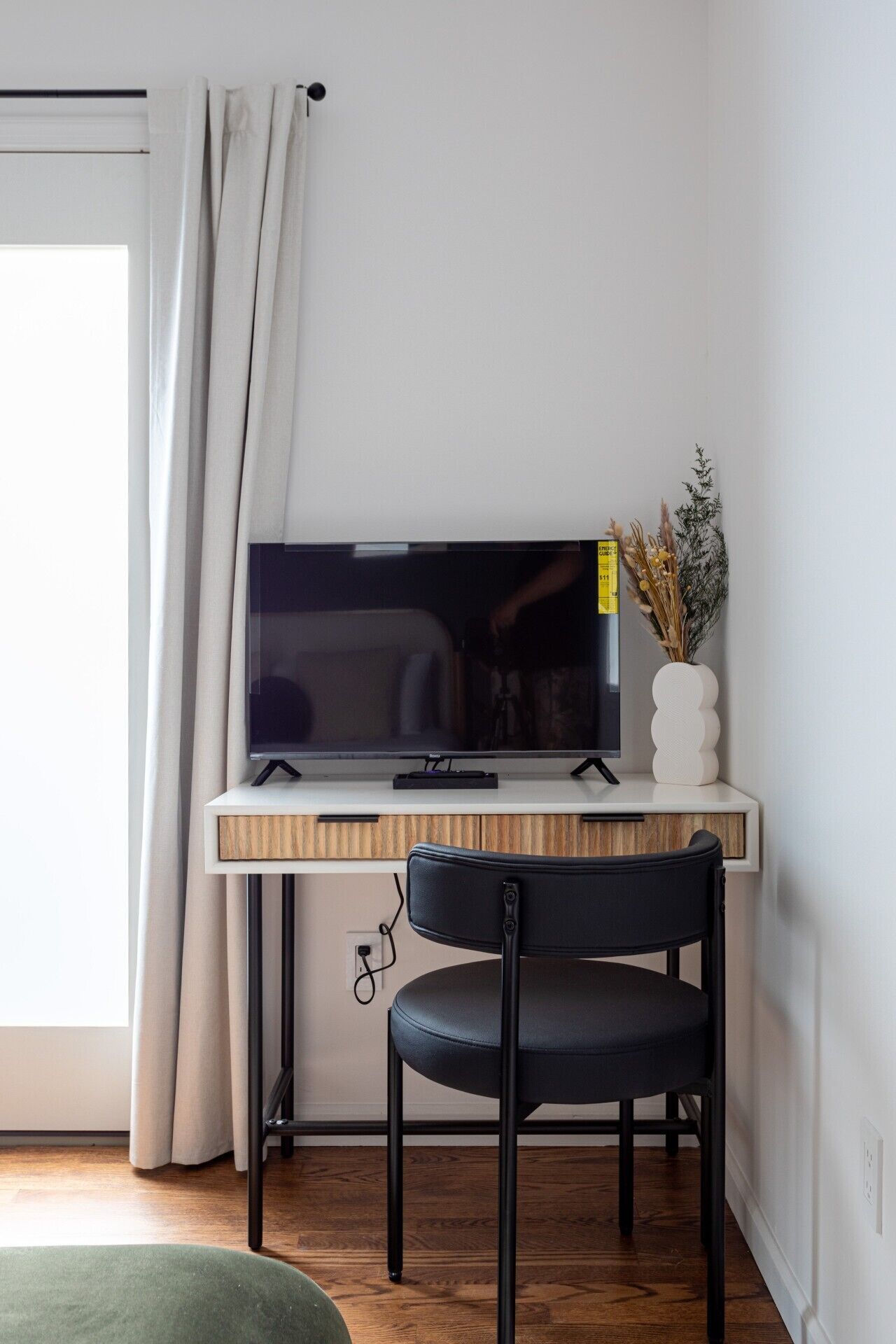 A modern room with a wooden desk, a flat-screen TV, a black chair, and a small potted plant.